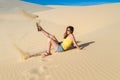 Woman sits on the sand in the desert, wearing a T-shirt and shorts