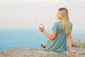 A woman sits on the seashore with glass in her hands.