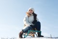 Woman sits and sledges from the mountain against the background of snow and sky in winterGirl laughs and rejoices in snow,