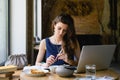 A woman sits at a table with books and a laptop in a coffee shop