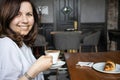 A woman sits at a table in a deserted cafe holding a cup of cappuccino