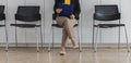 A woman sits waiting for a job interview, holding a job application, resume, application, she sits in a chair arranged in front of