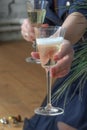 Woman sits on wooden floor holds glass of champagne and serves the second glass to viewer