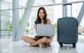 woman sitting on the airport floor, typing on her phone and laptop Royalty Free Stock Photo