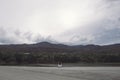 A woman sitting alone by the lake looking at the mountains with cloudy and gloomy sky Royalty Free Stock Photo