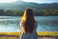 A woman sitting alone by the lake looking at the mountains with green nature