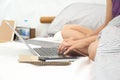 Woman sitting on bed in bedroom working with laptop computer