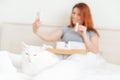 A woman is sitting in bed with a mobile phone in her hands. A white cat lies at the feet of the mistress with a cold Royalty Free Stock Photo