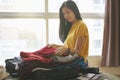 Woman sitting on bed and pack clothes in suitcase bag in bedroom, prepare for new journey and travel to long weekend trip Royalty Free Stock Photo
