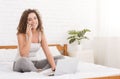 Woman sitting on bed, working on laptop and calling Royalty Free Stock Photo