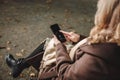 Woman sitting on bench in autumn park and using smart phone Royalty Free Stock Photo