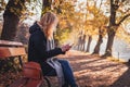 Woman sitting on bench in autumn park and using smart phone Royalty Free Stock Photo