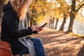 Woman sitting on bench in autumn park and using smart phone. Royalty Free Stock Photo