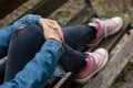 Woman sitting on a bench, holding her leg with her arms, with black ripped jeans and pink canvas sneakers