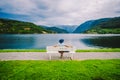 Woman sitting on a bench looking at the fjord in Ulvik, Norway. Fjord coastal promenade in Ulvik, Hordaland county, Norge. Lonely