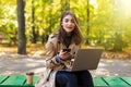 Young Woman sitting on bench in park use on cell phone and using laptop in autumn park Royalty Free Stock Photo