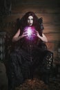 Woman sitting in a black, Gothic throne with a pink glowing orb in her hands Royalty Free Stock Photo