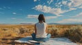 A woman sitting on a blanket facing away from the camera as writes in a journal surrounded by the peaceful stillness of