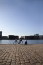 Woman sitting on boardwalk and looking out over the water in an urban harbor with a bicycle standing next to her. Royalty Free Stock Photo