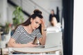 Woman sitting in a cafe in front of a laptop thinking about a problem with her hands touching head. Adult lady trying to