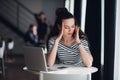 Woman sitting in a cafe in front of a laptop thinking about a problem with her hands touching head. Adult lady trying to