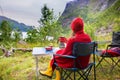 Woman, sitting on a camping chair in front of a tent, enjoying cup of coffee and amazing view in Norway Nordland, Senja island in