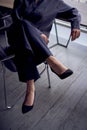 Woman sitting on chair with legs crossed over the armrest. High heels, black pants, silk blouse. Cityscape outside through window Royalty Free Stock Photo