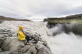 Woman sitting on the cliff edge next to Dettifoss waterfall in Vatnayokull national park, Iceland