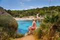 A woman sitting on a cliff, gazing at Cala Gat beach in Mallorca