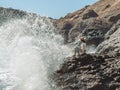 Woman sitting on cliff`s edge near sea with big splashes Royalty Free Stock Photo