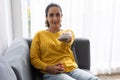 Woman sitting comfortable at home sofa watching tv pointing remote control for changing tv channel program Royalty Free Stock Photo