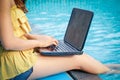 A woman sitting on a computer by the pool