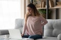 Woman sitting on couch near laptop suffers from back pain Royalty Free Stock Photo