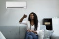 Woman Sitting On Couch Operating Air Conditioner Royalty Free Stock Photo