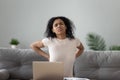 Woman sitting on couch touches lower back suffers from pain Royalty Free Stock Photo