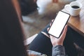 A woman sitting cross legged , holding black mobile phone with blank white desktop screen on thigh in cafe Royalty Free Stock Photo