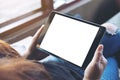 A woman sitting cross legged and holding black tablet pc with blank white screen on thigh in cafe Royalty Free Stock Photo