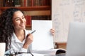 Woman sitting at desk, having videocall on laptop, holding paper Royalty Free Stock Photo