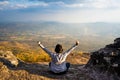 A woman sitting down with hands up on rocky mountain looking out at scenic natural view and beautiful blue sky Royalty Free Stock Photo