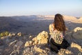 Woman sitting on the edge of a cliff, looking down toward the small crater valley in Israel