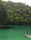 A woman sitting on the edge of a diving board in a magnificent green lagoon.