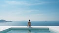 Woman sitting on the edge of swimming pool and looking at the sea