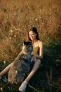 Woman sitting in a field with a dachshund dog smiling while spending time in nature with a friend dog in autumn at