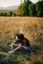 Woman sitting in a field with a dachshund dog smiling while spending time in nature with a friend dog in autumn at