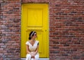 Woman sitting in front of the yellow door and orange brick wall Royalty Free Stock Photo