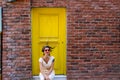 Woman sitting in front of the yellow door and orange brick wall Royalty Free Stock Photo