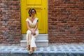 Woman sitting in front of the yellow door and orange brick wall Royalty Free Stock Photo