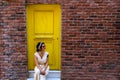 Woman sitting in front of the yellow door and orange brick wall Royalty Free Stock Photo