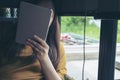 A woman sitting by glass window looking , using and holding tablet pc cover her face Royalty Free Stock Photo