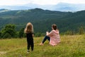 Woman sitting on grass and looking on mountains with child girl near
